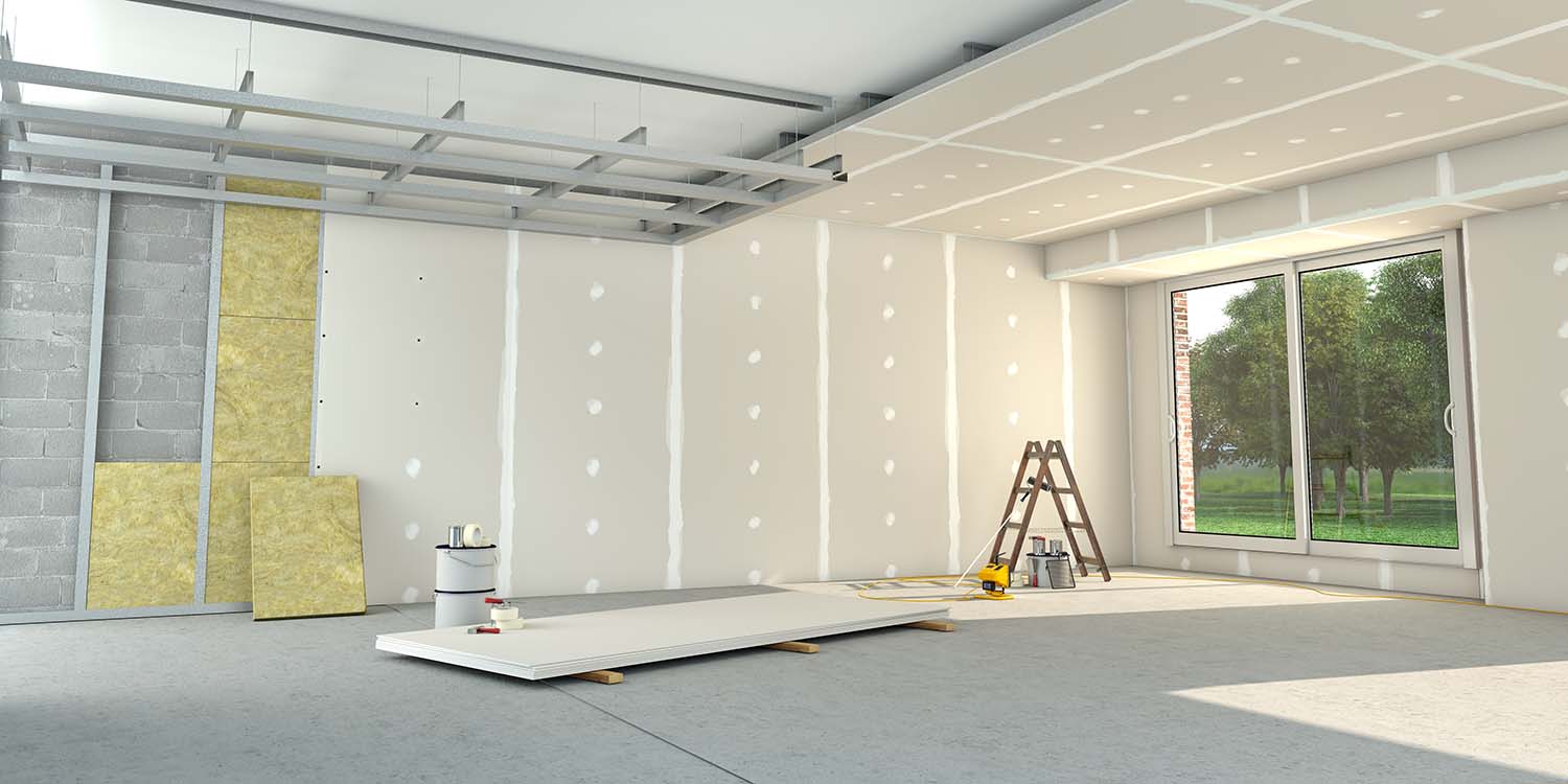 Das Bild zeigt einen Raum, der sich im Bau befindet. Die Wände sind noch nicht komplett verputzt und werden aktuell teilweise noch gedämmt. Im Raum stehen eine Leiter und mehrere Baumaterialien.